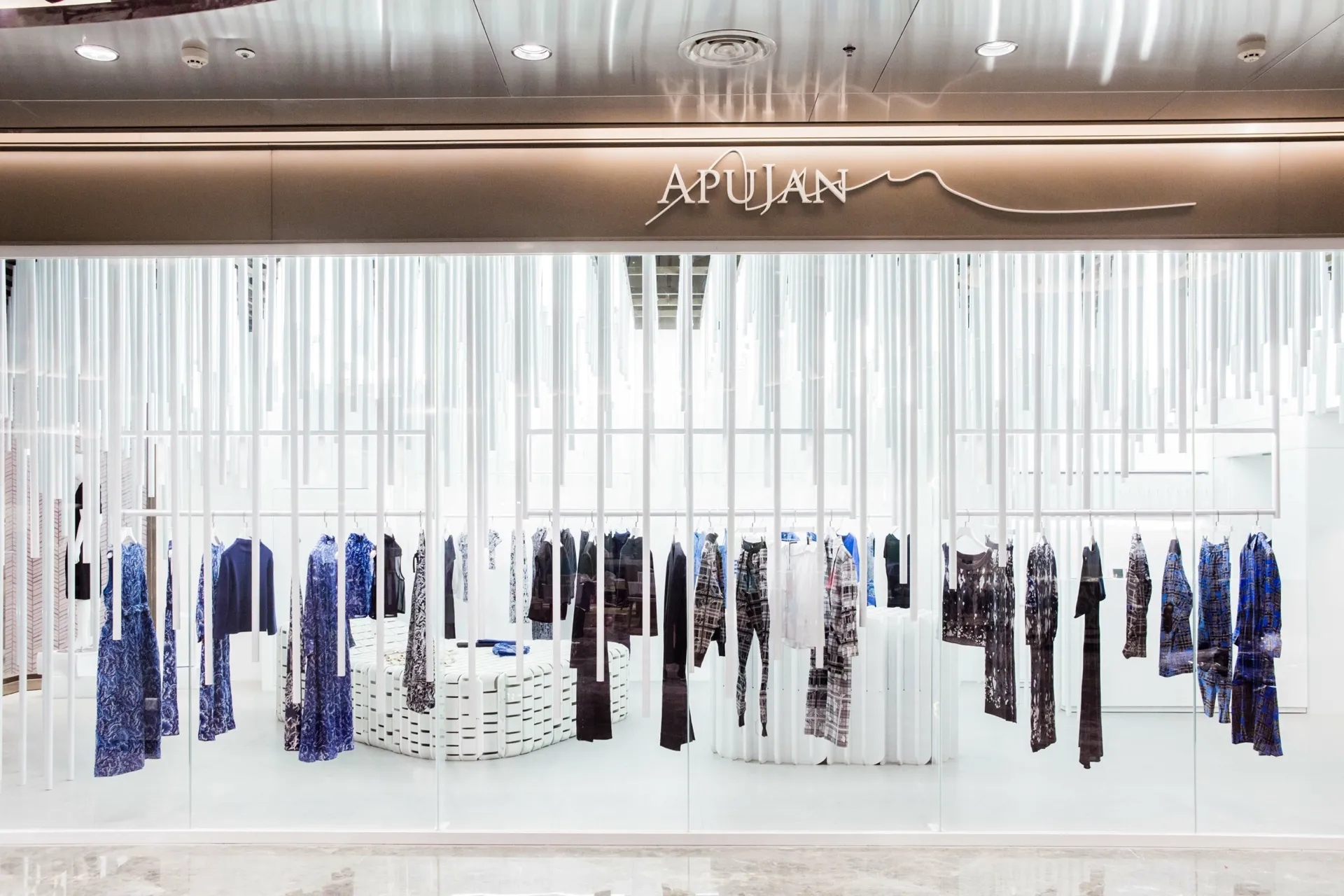 另外在專櫃的中央超過千片的客製化3D列印陶瓷桌面呼應地面的起伏，顏色與地磚使用大地色系水泥灰，讓地面起伏與漂浮曲面區別開來，燈光、烤漆鋁條及衣桿皆離開地面，潔白的空間加上垂掛的線性遮蔽讓消費者及店內展示的服裝從店外看來若隱若現，讓狹長的店面可以在空間中交織出不同的層次，使用者就像漂浮穿梭在另一個時空的感覺。