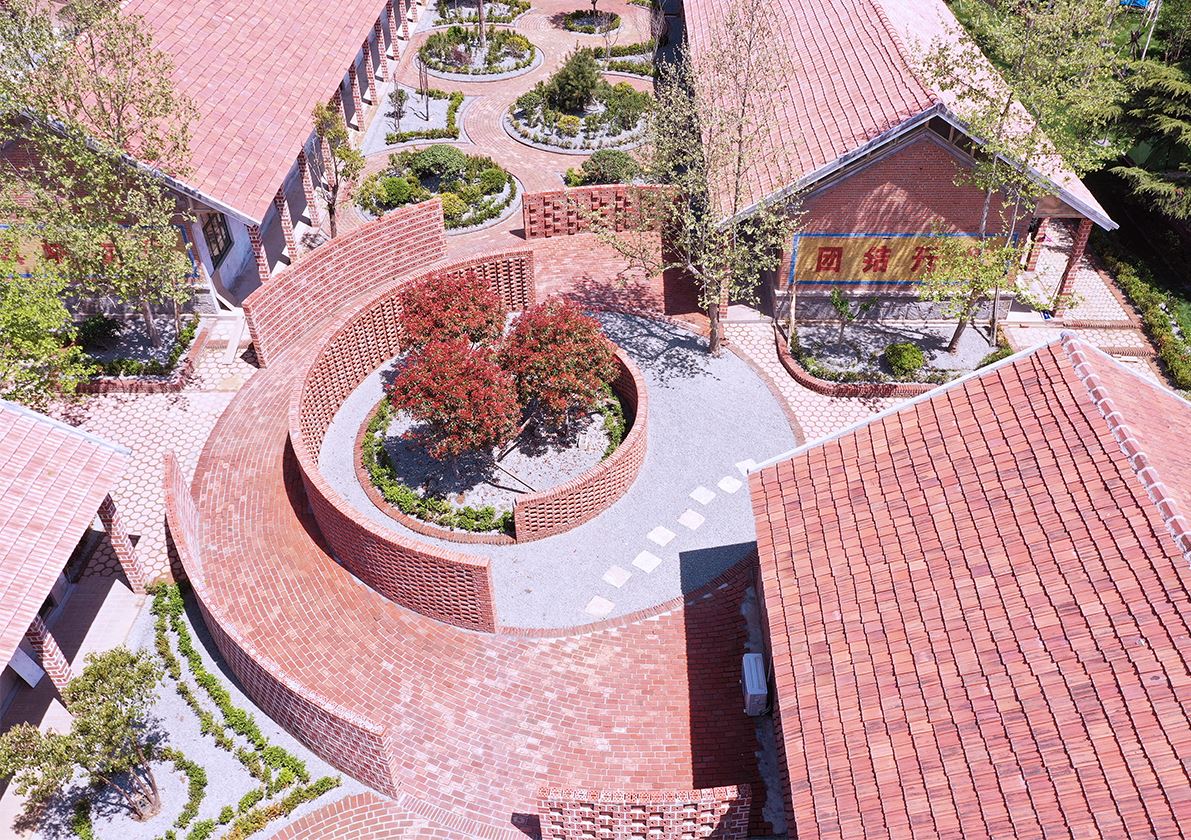 景观带用大小不一的圆将条形景观空间串联起来,形成三个不同的趣味景观场所--西侧下沉式的篝火聚会场所、中间环形小丘小道、东侧圆形迷宫墙。设计上继续沿用红砖作为建造的主材料来整合空间氛围,在尊重建筑现状的基础上运用圆形元素配置每个庭院入口的专属空间,增加其趣味性和体验性。